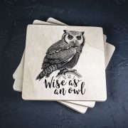 Balts krūžu paliktnis ar melnu pūces zīmējumu un tekstu: "Wise as an owl"