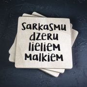 Balts krūžu paliktnis ar melnu tekstu: "Sarkasmu dzeru lieliem malkiem"
