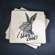 Balts krūžu paliktnis ar melnu zaķa zīmējumu un tekstu: 'Stay cool!"