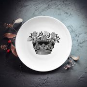 Mazais šķīvis ar melnu un sudrabotu kroņa zīmējumu.