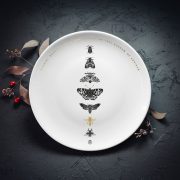 Vidējais šķīvis ar melnu kukaiņu zīmējumu un zelta elementu un tekstu: "Kukaiņi ragaiņi"